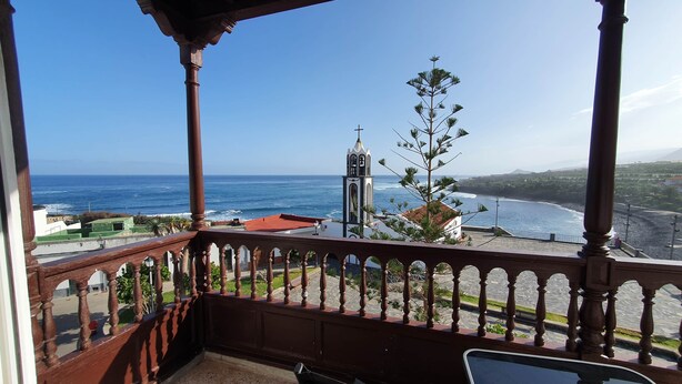 A balcony with a view of the ocean, a church tower, and a coastal landscape. - Apartamento vista Mar Caleta de Interián - Casa Oceano (La Caleta de Interián)