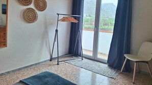 A room with a large window, a standing fan, a chair, and decorative wall hangings. - Apartamento vista Mar Caleta de Interián - Casa Oceano (La Caleta de Interián)