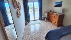 A bedroom with a bed, a dresser, a chair, and a view through a large window. - Apartamento vista Mar Caleta de Interián - Casa Oceano (La Caleta de Interián)