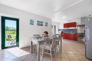 Eine moderne Küche mit roten Schränken, einem Edelstahlkühlschrank und einem Essbereich mit Tisch und Stühlen.