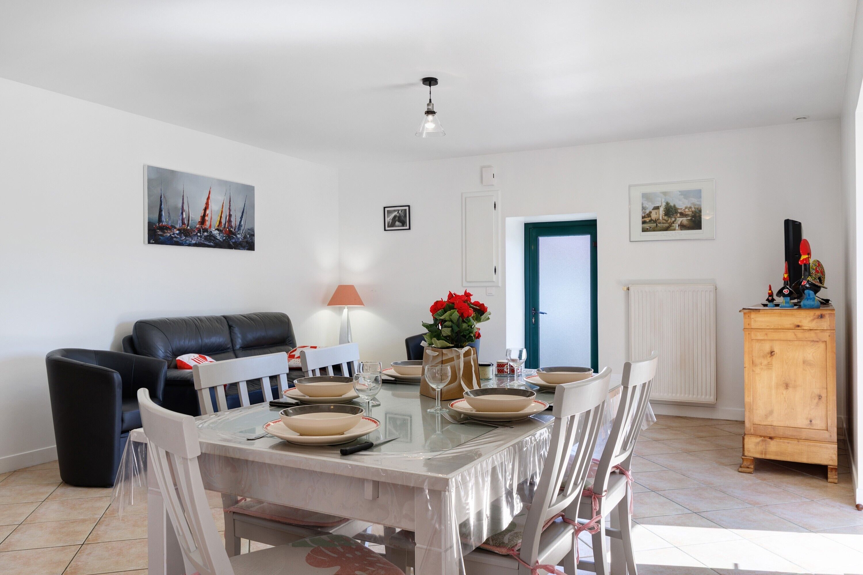 A dining area with a table set for four, a sofa, a cabinet, and artwork on the walls.
