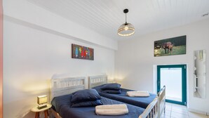 Un dormitorio con dos camas, una mesita de noche con lámpara, un accesorio de luz en el techo y una puerta que da a un balcón.