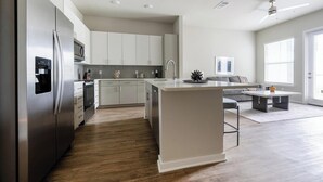Eine moderne Küche mit einer zentralen Kochinsel, Edelstahlgeräten und einem Essbereich mit grauem Sofa und Couchtisch.