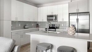 Une cuisine moderne avec des meubles blancs, des appareils en acier inoxydable et un îlot central doté de tabourets de bar.