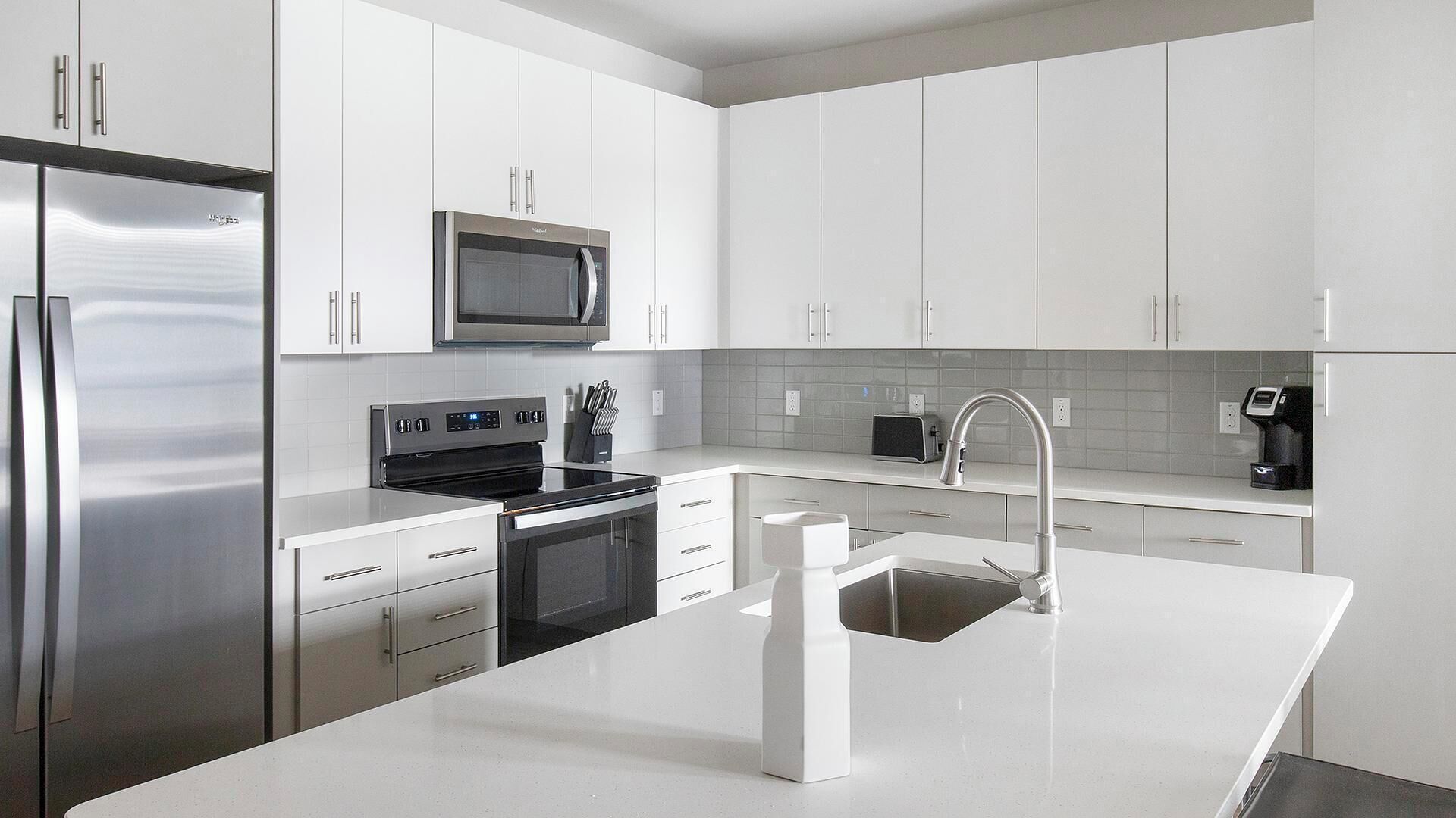 Een moderne keuken met roestvrijstalen apparatuur, witte keukenkastjes en een centraal eiland met een spoelbak.