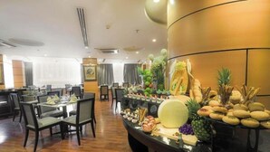 A hotel dining area with multiple tables and chairs, a buffet with various food items, and a large decorative wall. - Prestige Al Mashaer Hotel (Makkah)