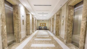 A long, marble-floored hallway with elevators on both sides, leading to a seating area with chairs and a table. - Prestige Al Mashaer Hotel (Makkah)