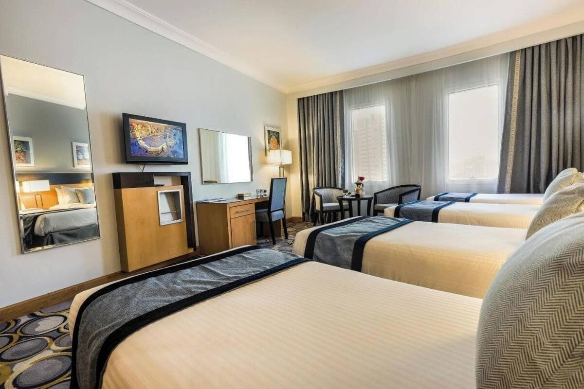 A hotel room with two beds, a desk, a chair, a TV, and a large window with curtains.