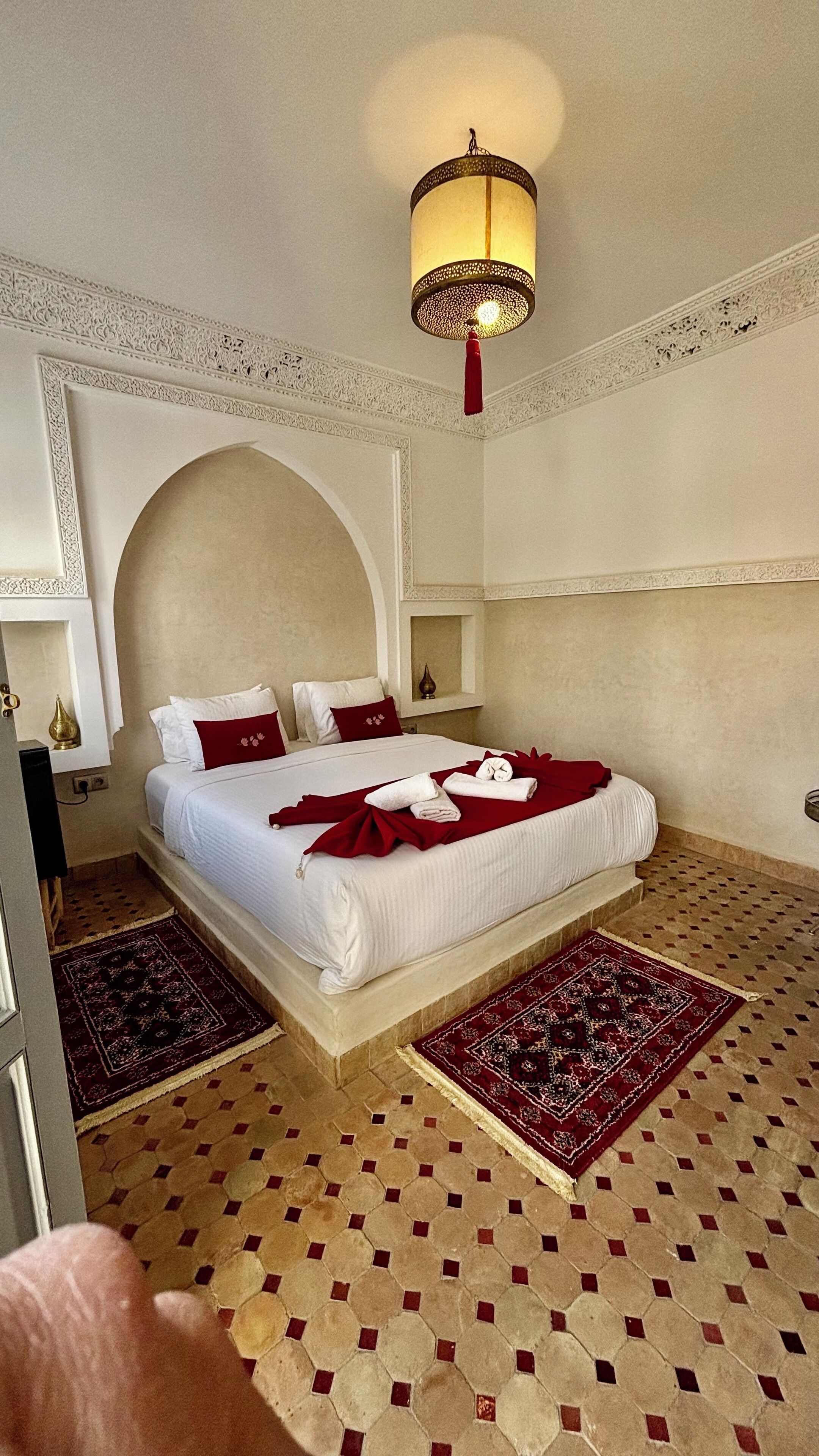 Une chambre d’hôtel avec un grand lit, un lustre décoratif au plafond et un sol à motifs.
