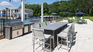 Patio esterno con barbecue, posti a sedere e ombrelloni.