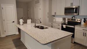 Cucina con mobili bianchi, piano di lavoro in granito, elettrodomestici in acciaio inossidabile e forno a microonde integrato.