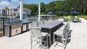An outdoor patio with a grill, seating, and umbrellas. - Landing | Modern 3BD, Gym, Pool (Newberry)