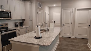 A kitchen with white cabinets, a granite countertop, stainless steel appliances, and a built-in microwave. - Landing | Modern 3BD, Gym, Pool (Newberry)