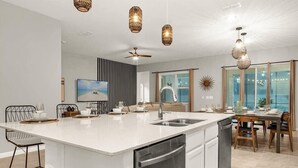 Une cuisine moderne dotée d’un grand îlot central, d’appareils électroménagers en acier inoxydable et de luminaires suspendus.