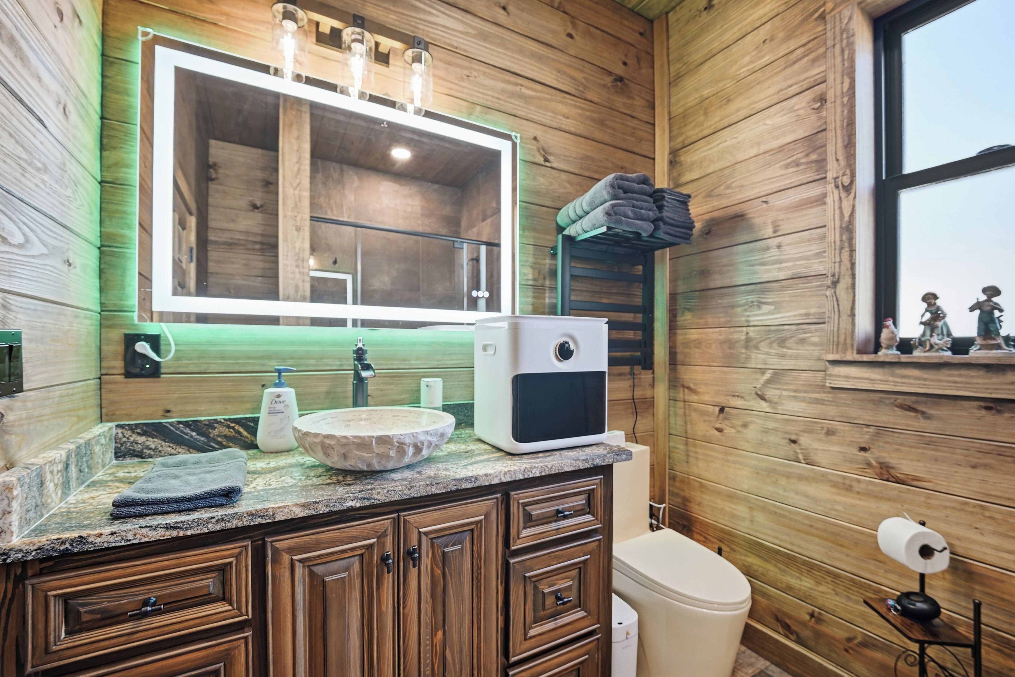 A wooden cabin bathroom with a large mirror, a sink, a toilet, and a window.
