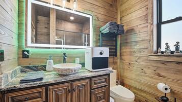 A wooden cabin bathroom with a large mirror, a sink, a toilet, and a window.