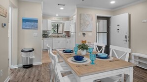 A dining area with a wooden table set for four, white chairs, and blue glassware. - Beautiful Condo-Pool Hot Tub Tennis Walk to Beach! (Hilton Head Island)