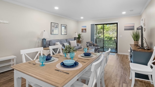 A dining area with a wooden table set for four, surrounded by white chairs. There is a sofa and a small cabinet in the background. - Beautiful Condo-Pool Hot Tub Tennis Walk to Beach! (Hilton Head Island)