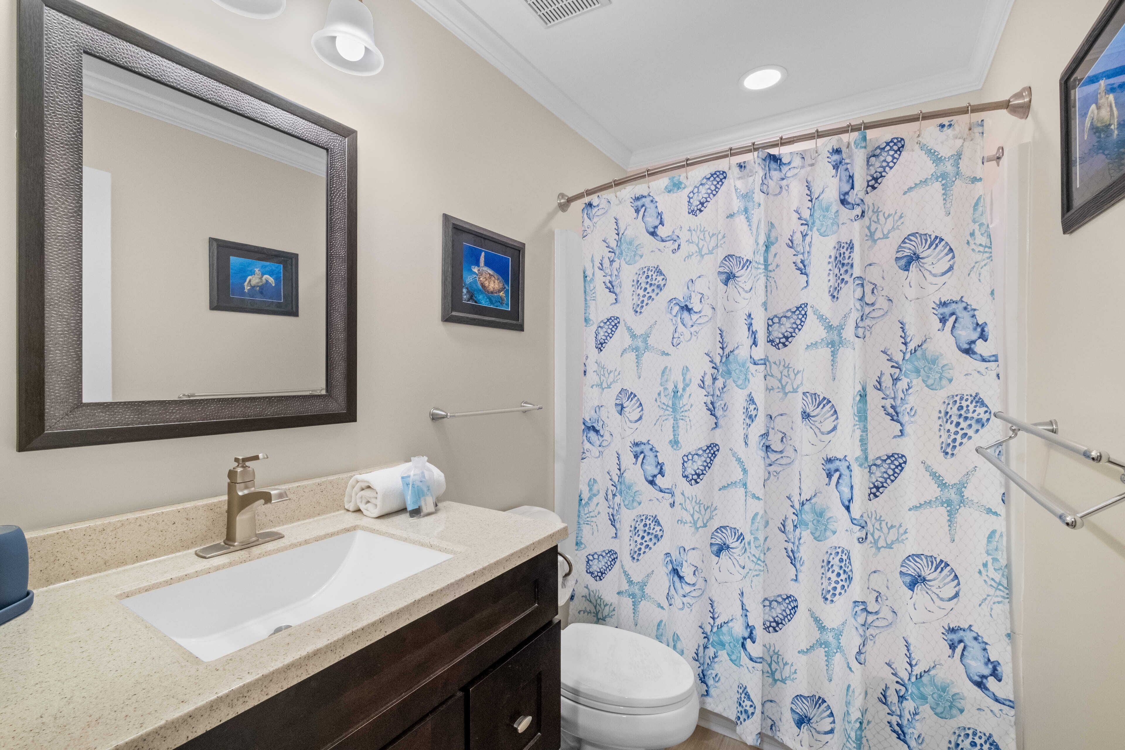A bathroom with a white sink, a mirror, a toilet, and a shower curtain with a blue sea life pattern.