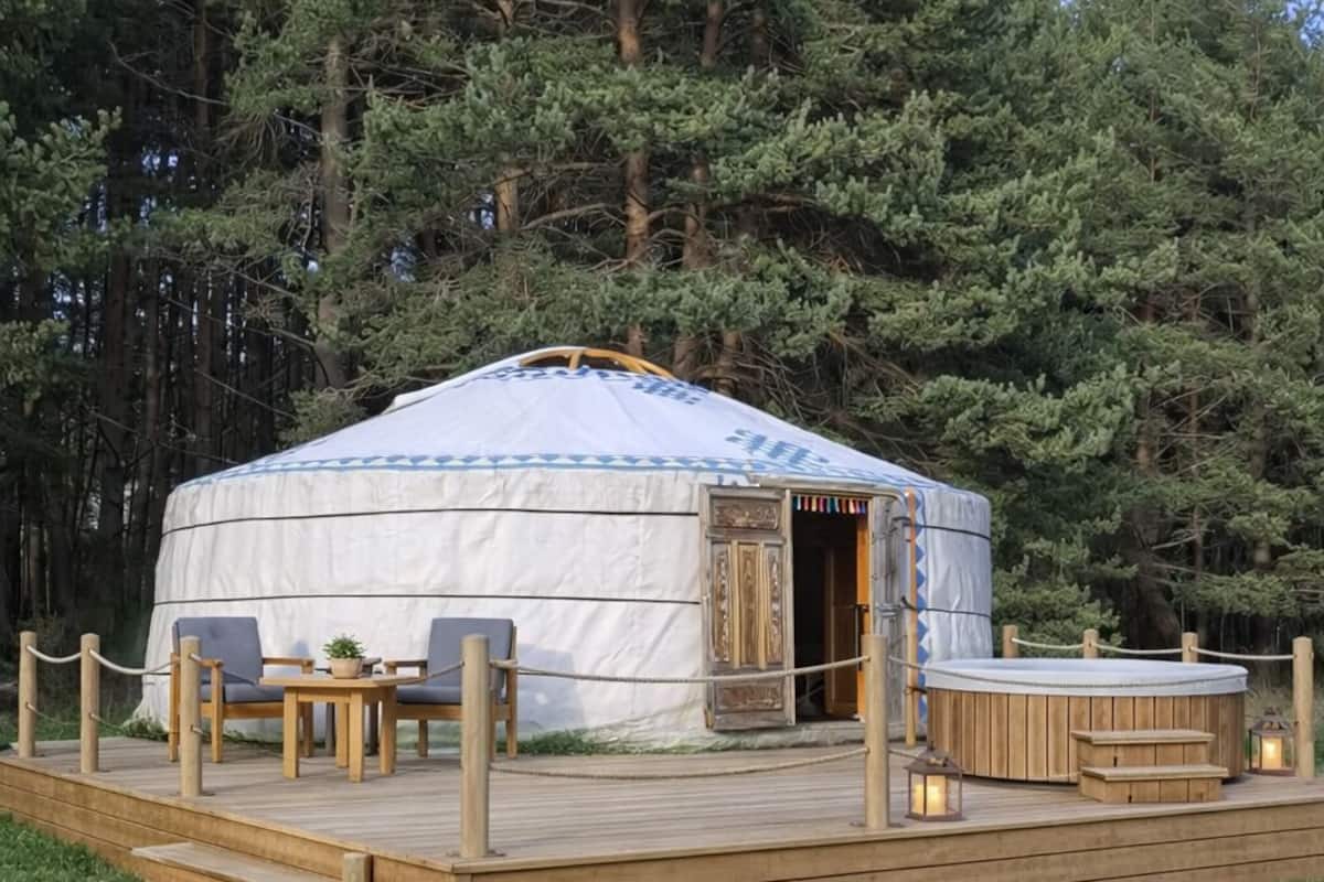 Una yurta con terraza de madera, zona de estar y jacuzzi.