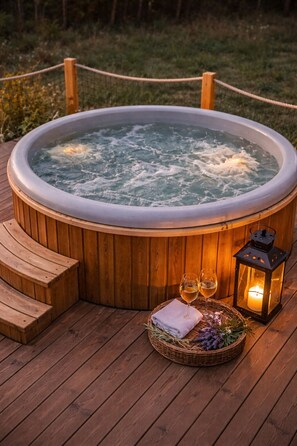 Ein Whirlpool, umgeben von einer Holzterrasse mit Sitzgelegenheiten, zwei Weingläsern und einer Kerze auf einem Tablett.