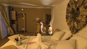 A hotel room with a large bed, a wooden headboard, a small table with a lamp, and a wall-mounted mirror. - Les insolites de la bastide (La Bastide)