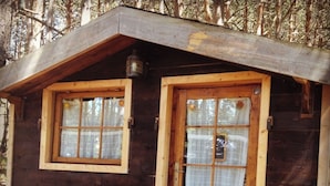 A small wooden cabin with a single door and two windows, each with a wooden frame and glass panes. - Les insolites de la bastide (La Bastide)