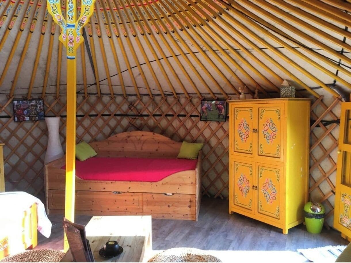Una habitación acogedora con una cama de madera, un armario amarillo y un techo de paja.