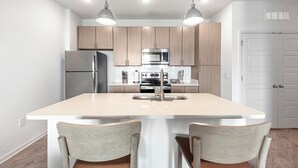Une cuisine moderne dotée d’un îlot central, d’appareils électroménagers en acier inoxydable et de meubles de rangement en bois clair.