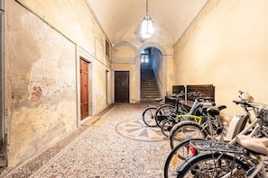 A hallway with a tiled floor, a staircase, and bicycles parked along the walls. - Atelier Lucca Centro – Historic Apartment in the Heart of the City (Lucca)