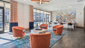 Un hall moderno con sillones naranjas, una mesa de centro y un área de comedor con una obra de arte geométrica en la pared.