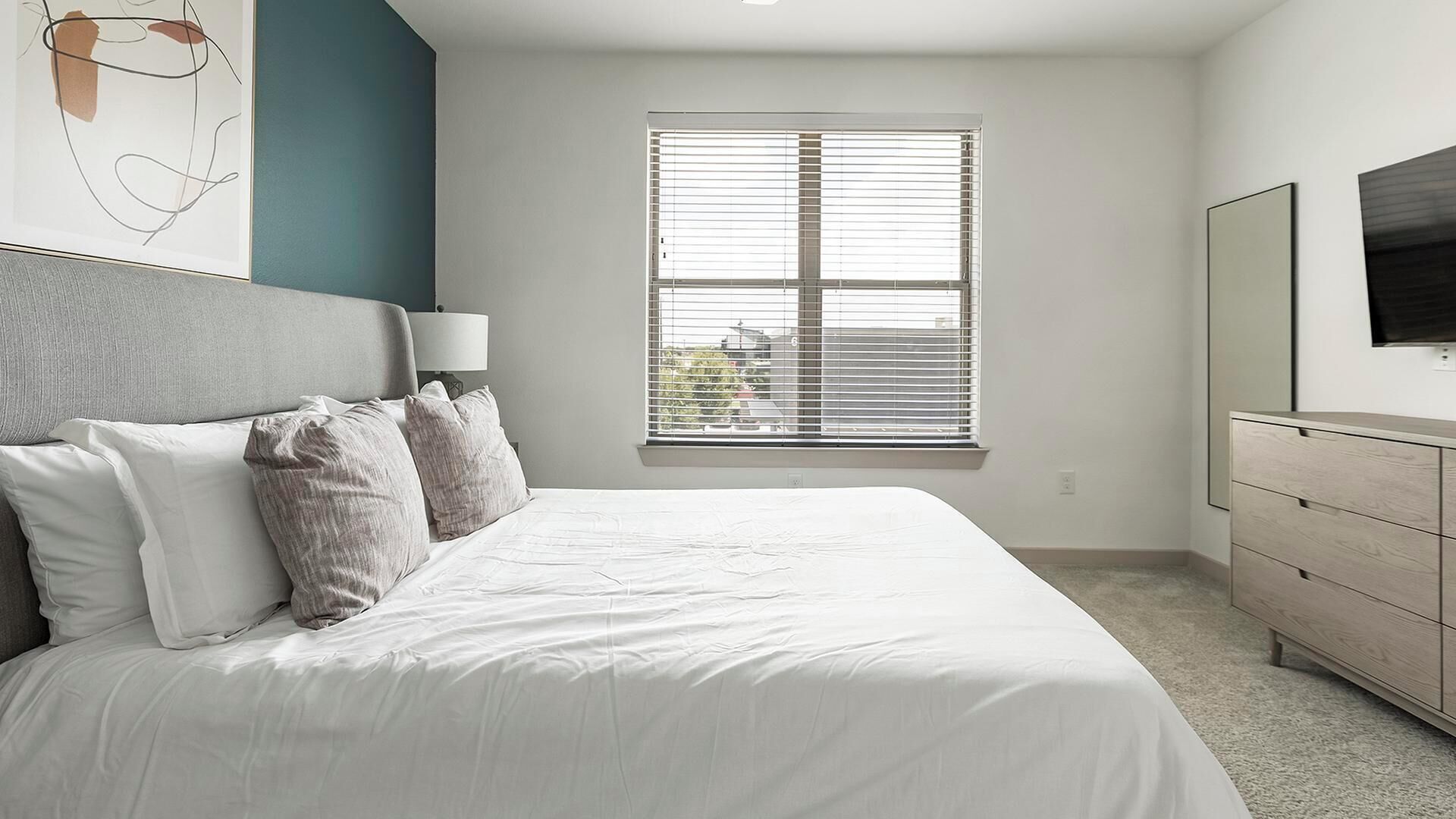 A modern bedroom with a large bed, a nightstand, a dresser, and a TV mounted on the wall.