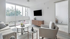 Ein modernes Wohnzimmer mit einer Couch, einem Sessel, einem Couchtisch und einem an der Wand befestigten Fernseher.