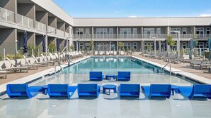 Ein Swimmingpool mit blauen Liegestühlen und ein Gebäude mit Balkonen im Hintergrund.