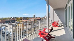 Ein Balkon mit roten Stühlen und einem Tisch, der auf einen Parkplatz und einige Gebäude blickt.