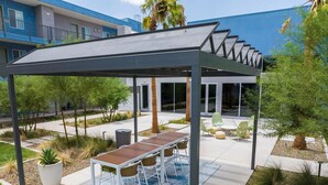 Een terras buiten met een pergola, een eettafel en stoelen.