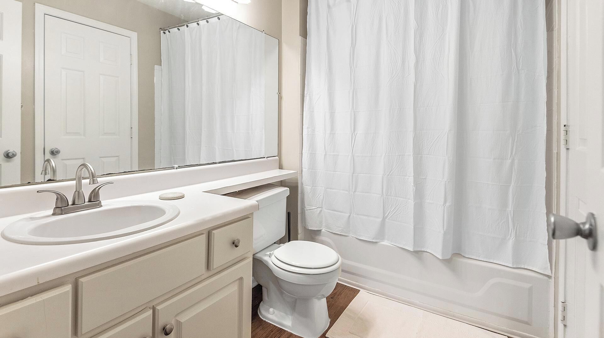 Un bagno con un lavandino bianco, due rubinetti, un water e una tenda per la doccia.
