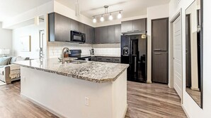 A modern kitchen with a granite countertop, stainless steel appliances, and a built-in oven. - Landing | Stunning 1BD, Gym (Glendale)