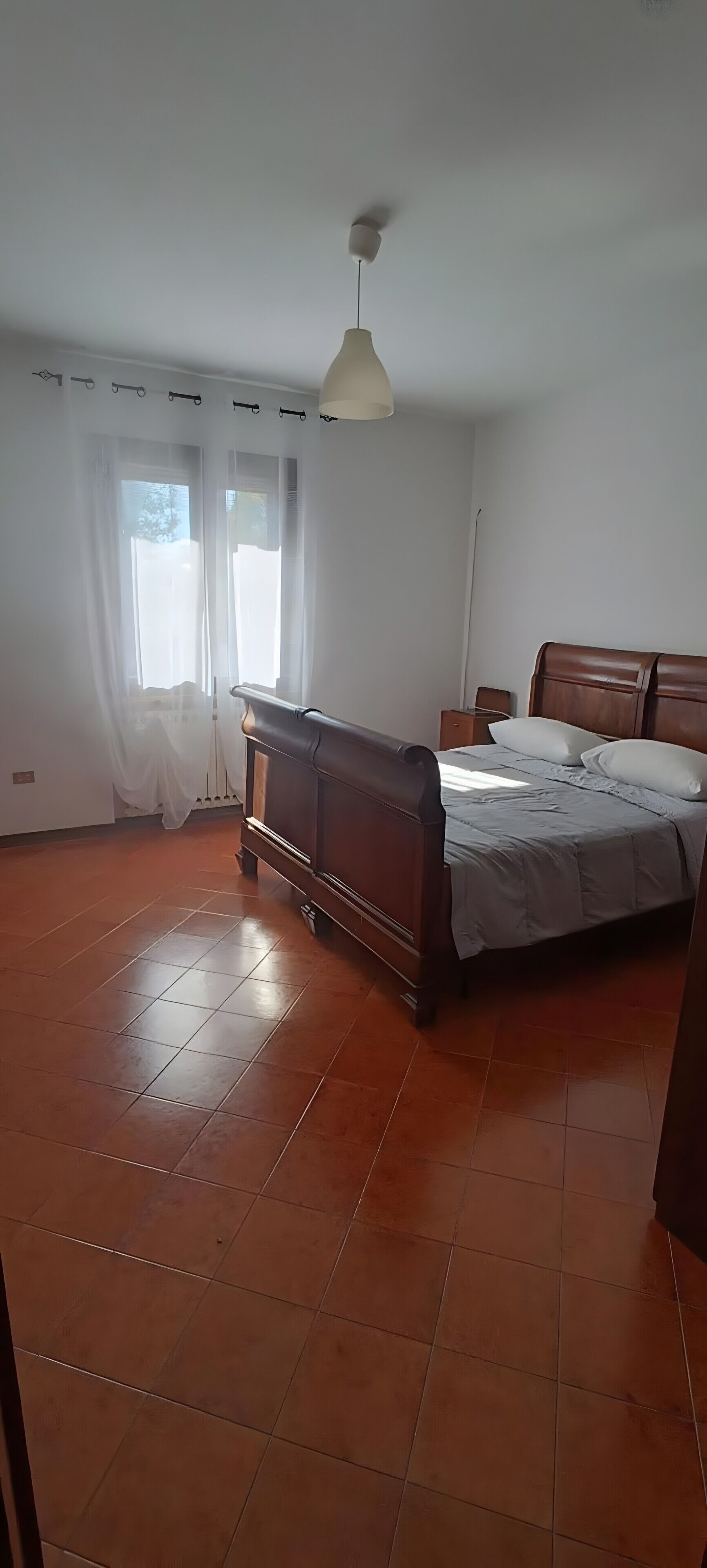 Un dormitorio con una cama de madera, una mesita de noche, una lámpara colgante y una ventana con cortinas.