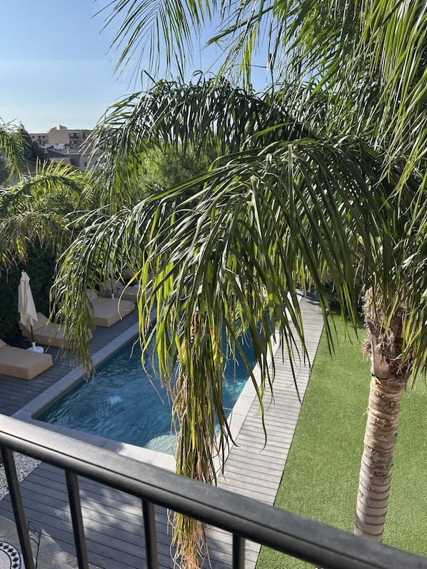 Área de piscina com palmeiras, espreguiçadeiras e um céu azul límpido.