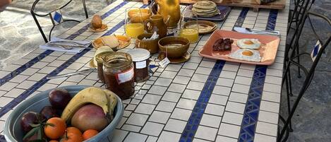 A breakfast setup with various foods and drinks on a tiled table outdoors.