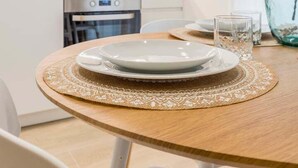 A modern kitchen with white cabinets, a built-in oven, and a dining area with a round wooden table set for two. - GuestReady - Modern and Cozy studio in Madrid (Madrid)