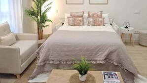 A modern bedroom with a large bed, a bedside table, a chair, and a potted plant. - GuestReady - Modern and Cozy studio in Madrid (Madrid)