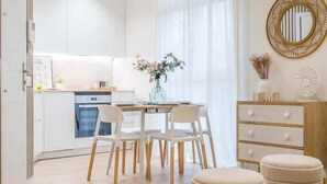 A modern kitchen with white cabinets, a dining area with a table and chairs, and a decorative mirror on the wall. - GuestReady - Modern and Cozy studio in Madrid (Madrid)