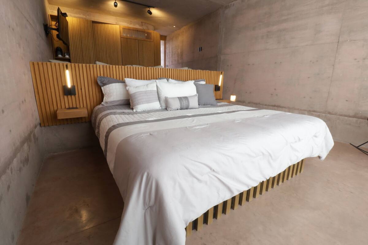 Ein modernes Schlafzimmer mit einem hölzernen Kopfteil, einem großen Bett mit vielen Kissen und integrierter Beleuchtung.