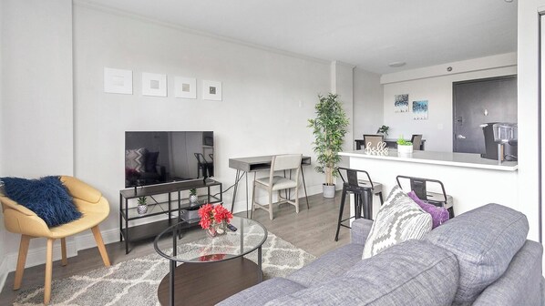 Un salon moderne comprenant un canapé, une table basse, un téléviseur et un coin repas avec des chaises et une plante.
