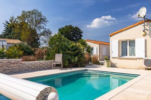 Une piscine avec un mur en pierre, une chaise et un bâtiment équipé d’une antenne parabolique.