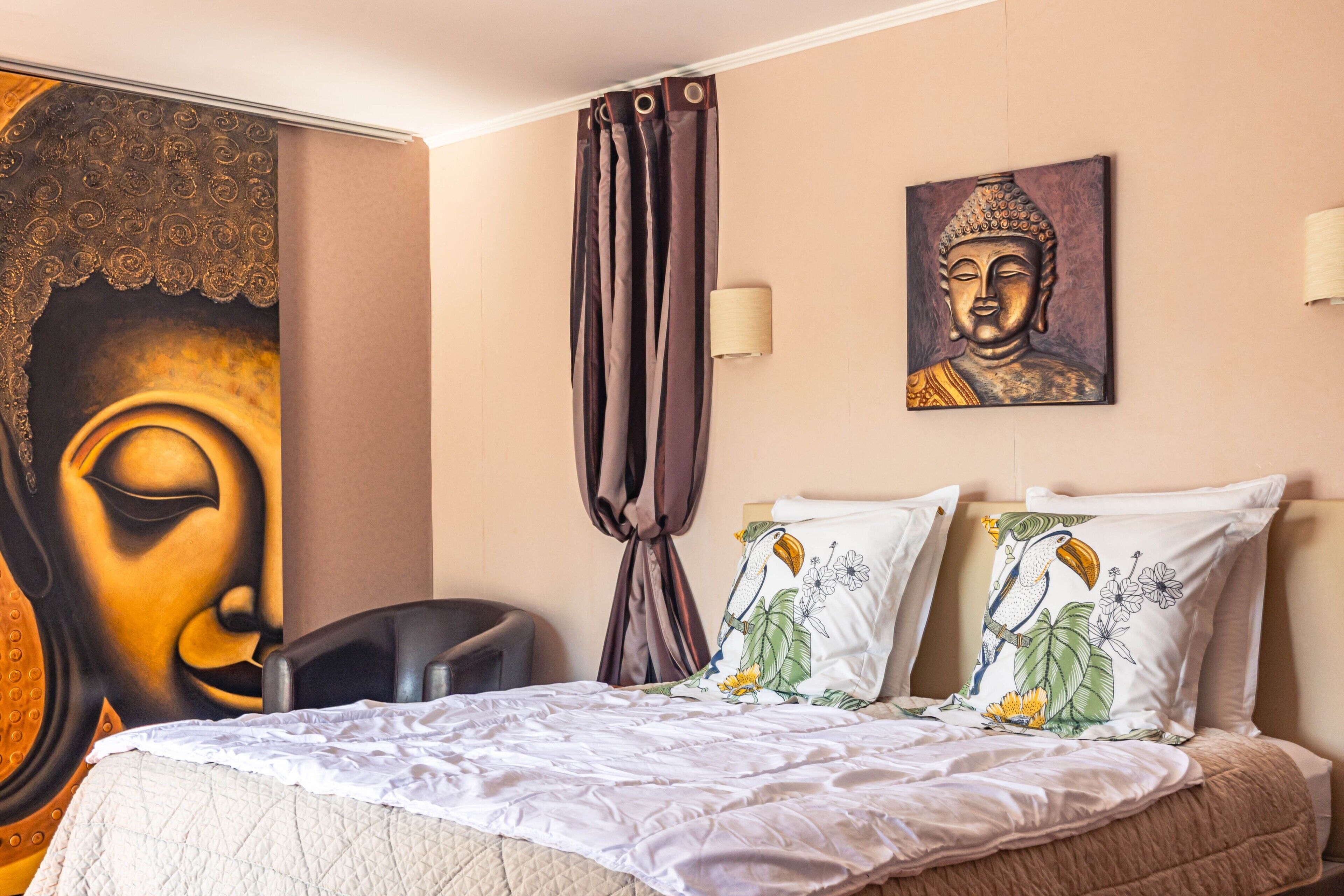 Una habitación de hotel con una cama, una silla, una cortina, un cuadro en la pared y una lámpara de pared.