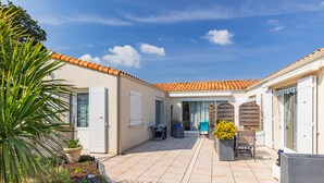 A courtyard with a tiled floor, a palm tree, a chair, a table, and a potted plant. - Guest Room “Dakar” with Shared Pool, Wi-Fi, and Air Conditioning (Saint-Pierre-d'Oléron)