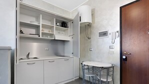 Una cocina compacta con armarios blancos, un lavamanos, una pequeña mesa con taburetes y una puerta de madera.